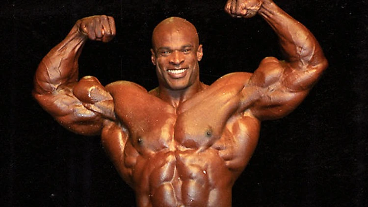 A bald bodybuilder flexes his biceps and muscles against a black background.