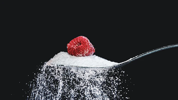 A spoon full of sugar with a berry on top and spilling sugar everywhere.