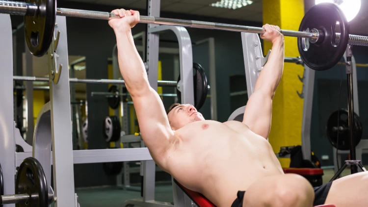 An image of a white man performing an incline bench press exercise at the gym, he is lying on a bench with his feet planted on the ground and his hands gripping a barbell above his chest.