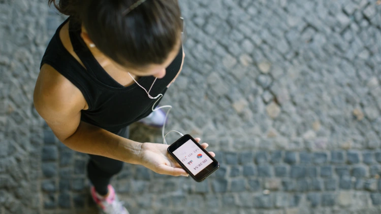 A woman in black top with earphones on her head while holding a phone and tracking her workout progress.