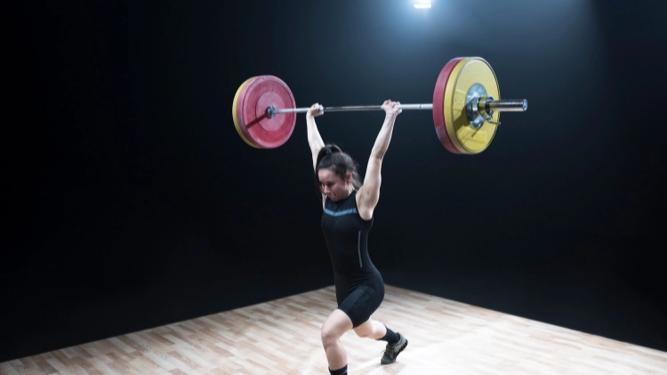 Woman in black gym clothes doing weightlifting with yellow and red weights color in a plain black background.