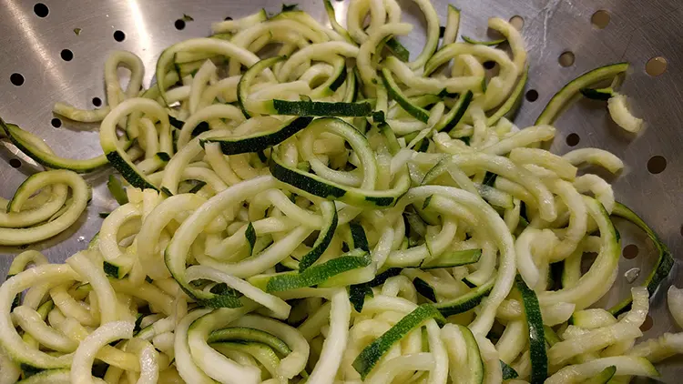 Zucchini noodles in a metal strainer.