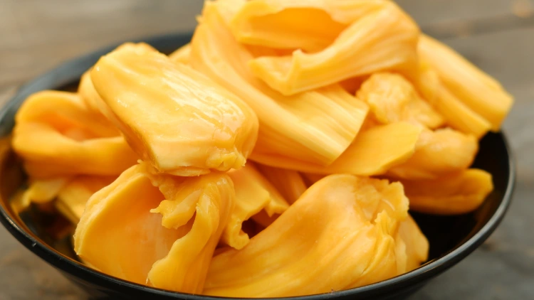A colorful bowl of fresh jackfruit pieces, with a mix of orange and yellow flesh, the jackfruit pieces are arranged in a mound, with the jagged edges of the fruit visible on some of the pieces, the bowl is set against a plain background, highlighting the natural beauty of the fruit, the jackfruit looks juicy and ripe, with a slightly sticky texture.