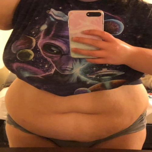 A woman wearing a black shirt and undergarments taking a mirror shot revealing her belly with excess fats.