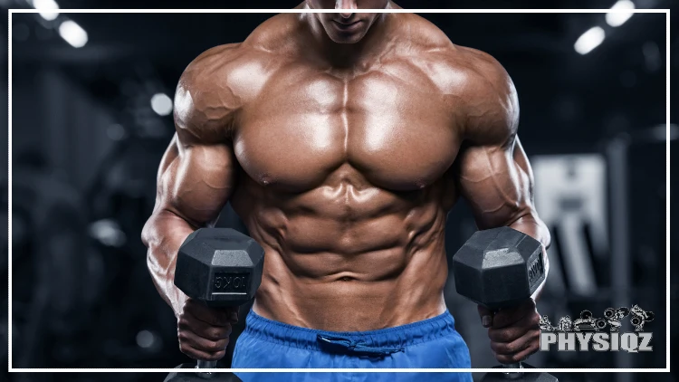 A topless man wearing blue shorts flexing his abs while holding a heavy dumbbell with both hands, his muscular arms showcase visible veins, set against a blurred gym background.