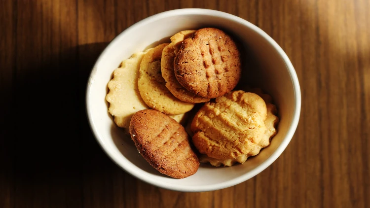 A selection of golden-brown, round, soft, and chewy cookies is displayed in a white bowl on a wooden surface.