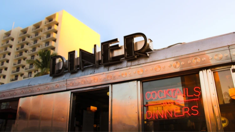 A black-colored diner logo with a yellow building and blue sky in the background.