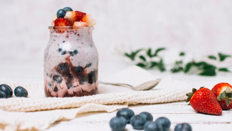 A refreshing blueberry and strawberry smoothie, poured into a clear glass cup and topped with fresh fruit, the smoothie is a vibrant purple and pink color, with small pieces of blueberries and strawberries visible in the drink, the glass is garnished with strawberry and blueberry.