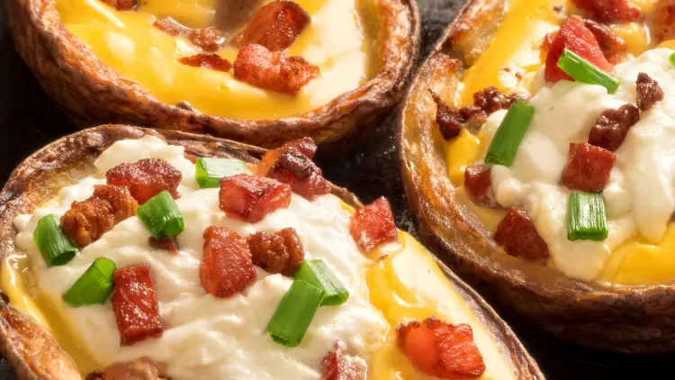Baked potatoes with a brown skin, sliced open to reveal the fluffy white interior, topped with melted cheese, crispy bacon pieces, and a sprinkle of finely chopped chives arranged in a visually pleasing manner, creating a contrast of colors and textures against the potato's smooth surface.