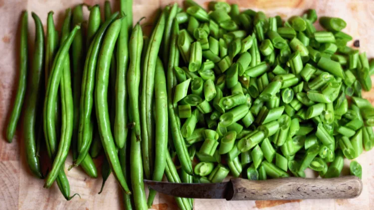A pile of chopped and fresh green beans is placed on a wooden board in the background, along with a knife with wooden handle.