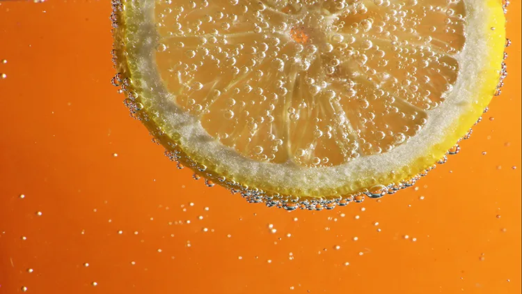 A bubbling slice of lemonade in a clear water with orange background.