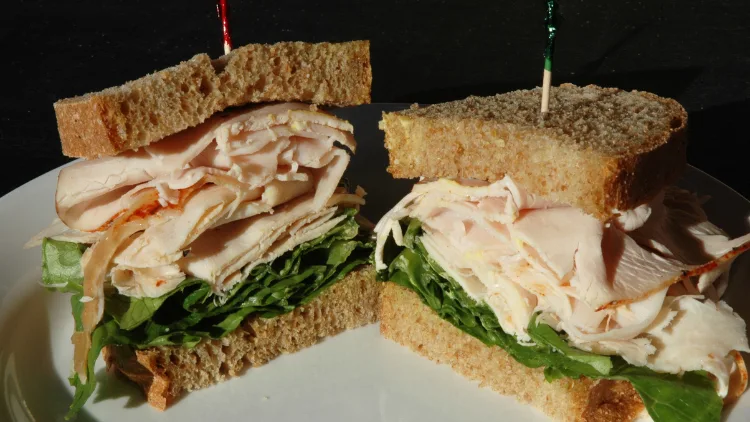 A healthy turkey sandwich made with lettuce and turkey meat, and then sliced in half, and pierced with a toothpick to keep everything in place and served on a white dish.