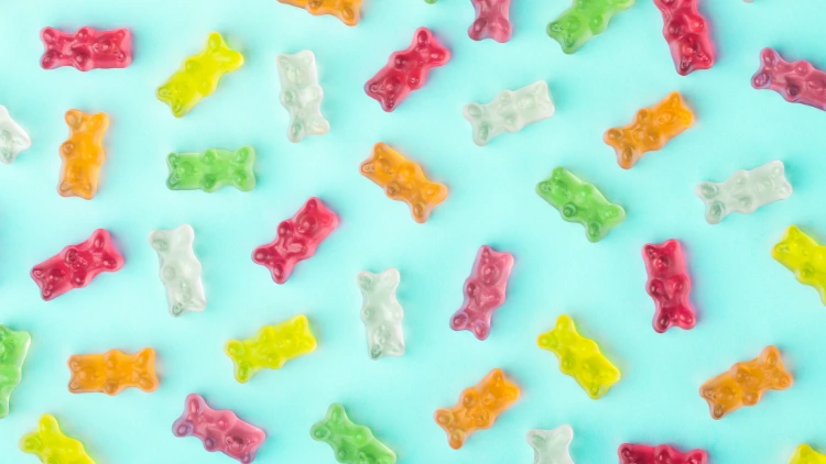 A variety of gummy bears in different colors set against a light blue background, the gummy bears are pink, green, clear, orange, and yellow, they are all the same size and shape, with a soft and chewy texture, the colors are bright and vibrant, and the bears are arranged in a random pattern.