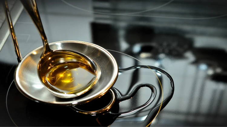 Palm oil is poured from a gold-colored ladle, with part of the oil spilling onto a dark kitchen counter.