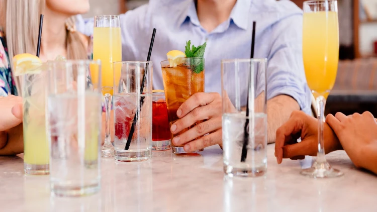 Five drinking glasses filled with various drinks, each with a different color and texture, two champagne glasses with yellow-colored drinks are also visible in the image, the drinks appear to be refreshing and enticing, with a range of colors from clear to dark shades.