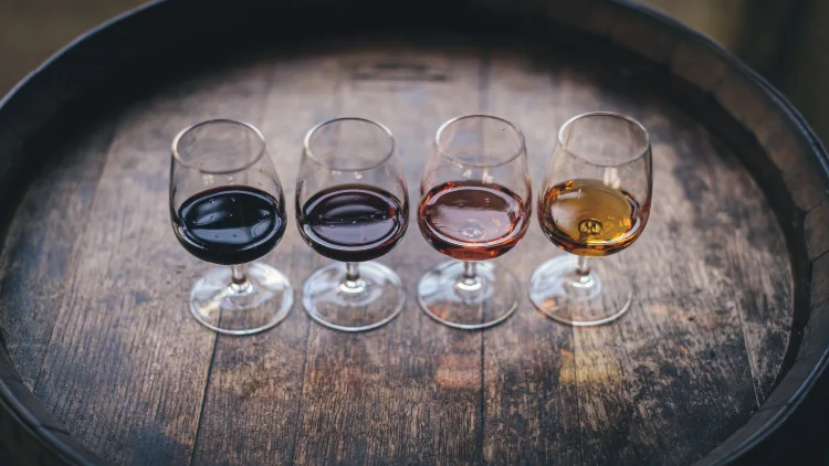 Four wine glasses filled with different flavors of wine displayed on top of a wooden wine table.
