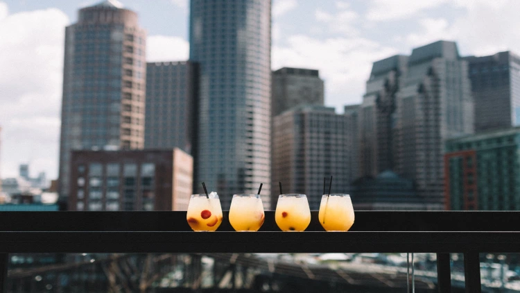 Four drinks placed on a flat surface in front of a city skyline view in the background.