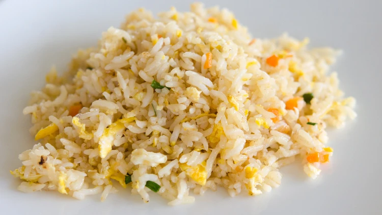 A serving of fried rice made with a mix of ingredients such as rice, onions, and eggs served on a white plate.