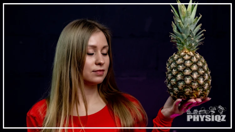 A young woman wearing a red top stands in peaceful contemplation about "Is pineapple keto friendly or not" and has eyes closed, a red shirt, blonde hair and is cradling a pineapple in her left hand.