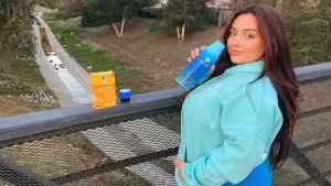 A woman wearing a a blue jacket wondering is Liquid IV keto as she holds a blue Liquid IV tumbler, bridge with nature background.