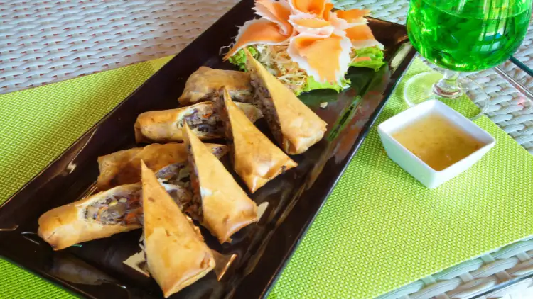 A plate of fresh Thai spring rolls stuffed with veggies and herbs, presented on a rectangular white platter with dipping sauce to accompany the rolls.