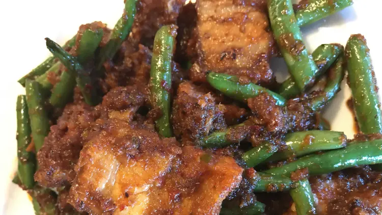 Close up of a red curry stir fry with green beans served on a white plate.