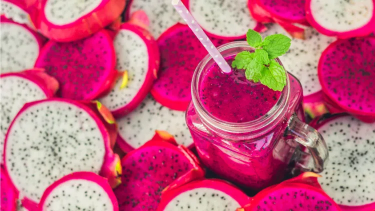 A refreshing pink dragon fruit smoothie served in a clear glass with a straw, garnished with mint leaves in sliced pink and white dragon fruit arranged on a background.