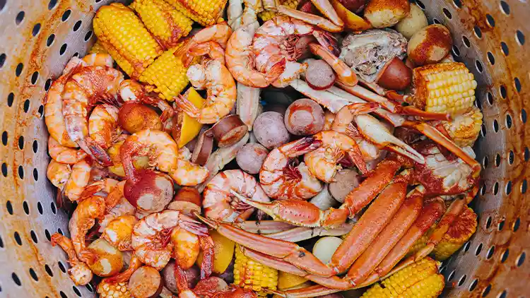 A seafood boil that includes crabs, shrimps and corns, served in a plastic container with drainage holes.