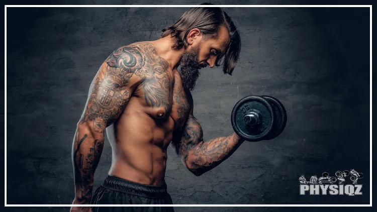 A shirtless muscular, bearded male with a tattoo on his torso doing a shoulder and bicep workout with dumbbell over dark grey background.