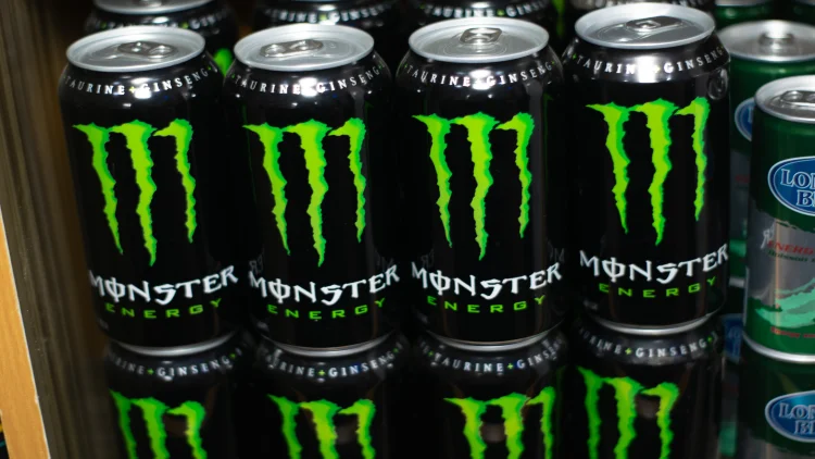 A stack of Monster energy drink cans, arranged in a neat and orderly pile, with the recognizable green 'Monster' logo prominently displayed on each can.