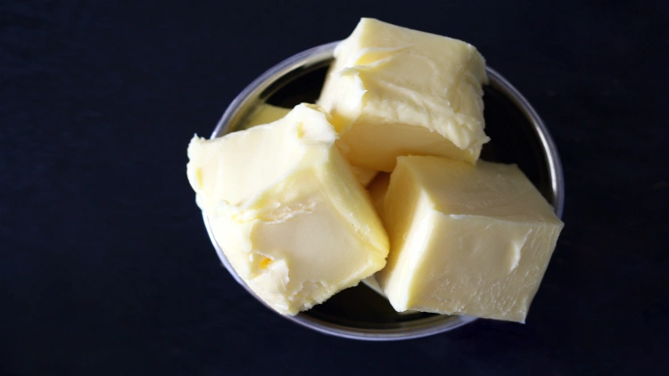 Three small cubes of butter are arranged in a clear glass bowl, set against a black background.