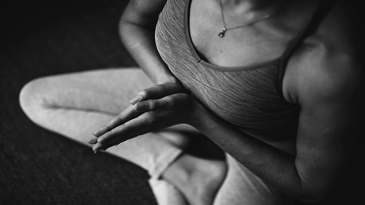 A black and white photo of a woman wearing a tank top and leggings, meditating with her arms put together.