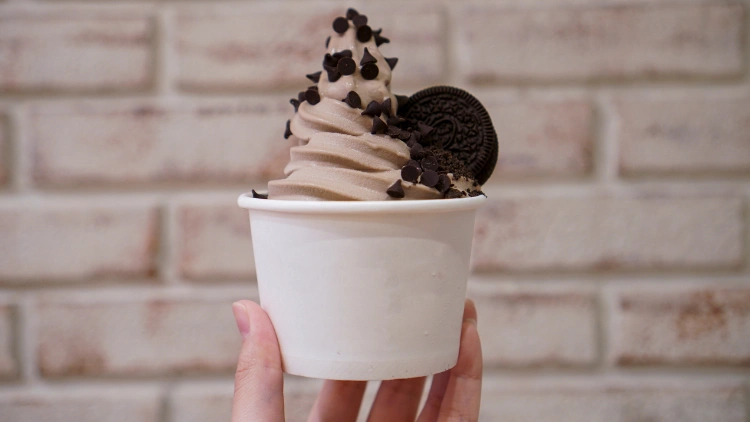 Chocolate frozen yogurt in a paper cup, topped with chocolate oreo biscuit.