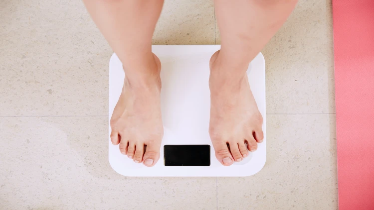 A bare foot resting on a white digital weighing scale with no weight displayed on the screen.