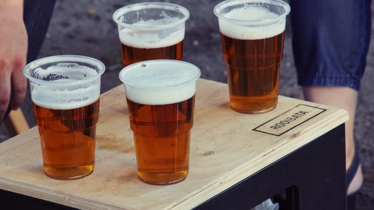 Four beers filled in a clear plastic cup, showcasing their golden colors and bubbly foam.