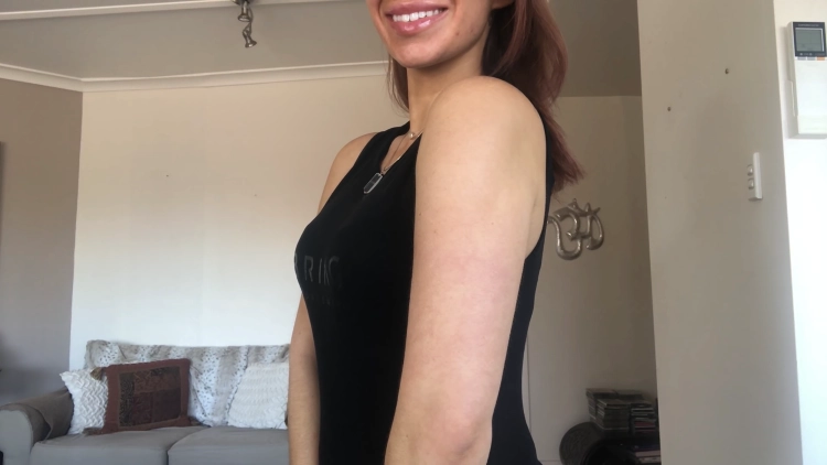 A young woman with a black sleeveless top, smiling towards the camera while showing her skinny, lean arm, the woman's posture is confident and relaxed, and she appears comfortable in her own skin.