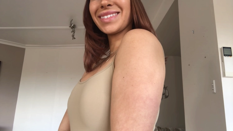 A young woman with a genuine smile on her face, looking towards the camera while showcasing her lean arm.