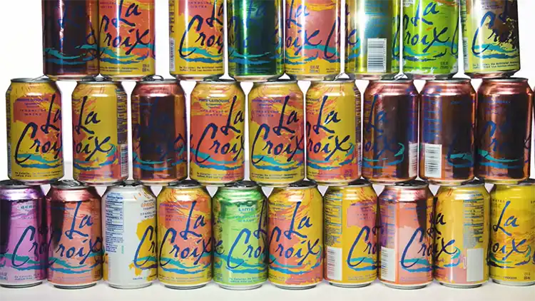 Twenty-seven cans of LaCroix sparkling water that comes in different variation such as Pamplemousse, peach-pear, berry, and keylime, arranged in a three-layer stack and displayed on a white surface against a white backdrop.