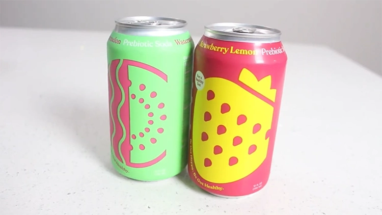 Two cans of Poppi prebiotic soda in different flavors such as strawberry lemon in pink can and watermelon in light-green can displayed on top of a white shiny surface.