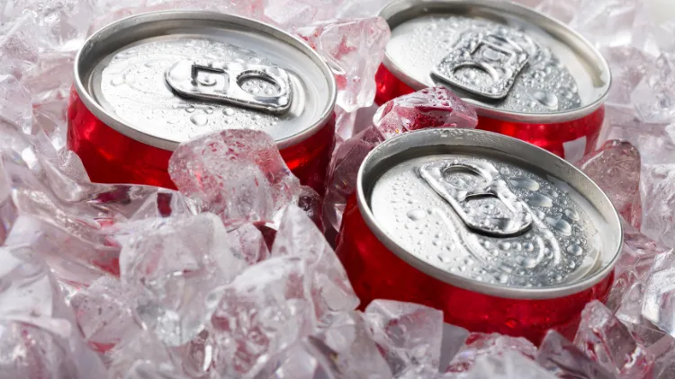 Three red unopened cans of carbonated soda stuck in a space filled and surrounded with lots of ice cubes.