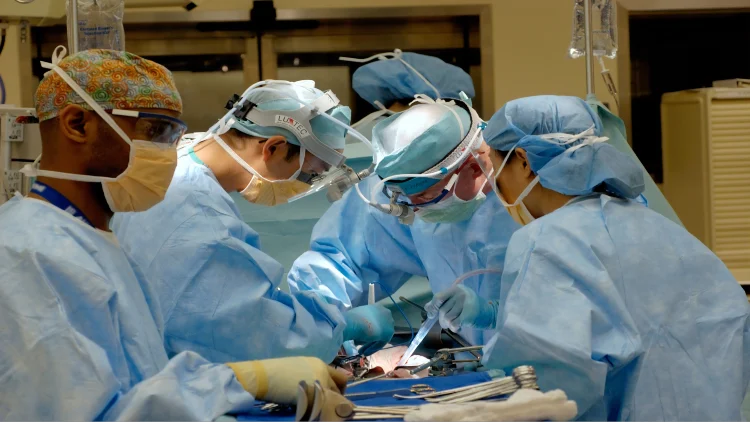 A team of surgeons performing a surgery in an operating room, wearing surgical scrubs and using medical instruments while attending to the patient on the operating table.