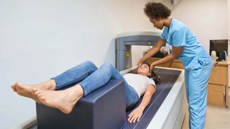 A nurse wearing medical scrubs preparing a woman for a bone density scan, positioning her on the scanning machine.