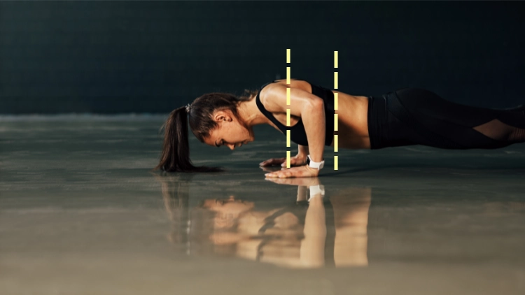 A woman wearing a black tank top and black pants is in a dimly lit gym with shiny reflective floor doing pushups exercise.