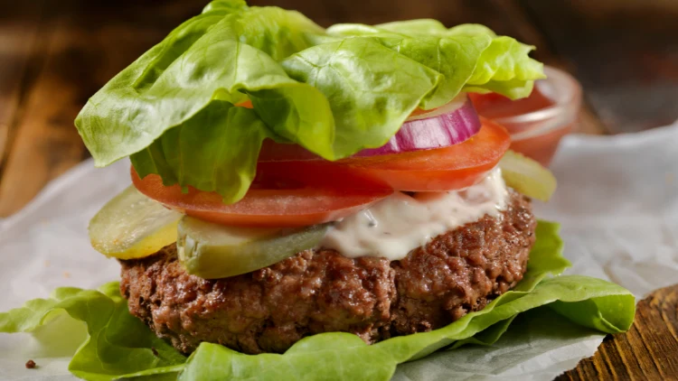 A healthy bunless burger featuring a juicy grilled patty topped with sliced onions, fresh tomatoes, crisp pickles, and a creamy white sauce, this burger is a great low-carb and high-protein meal option, packed with flavor and nutrition, perfect for those looking for a healthier twist on a classic burger.