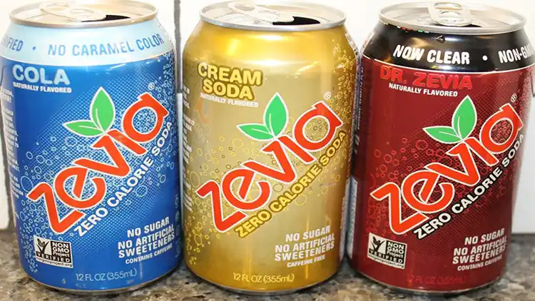 Three opened cans of Zevia zero calorie soda that comes in three different flavors such as cola in blue color, cream soda in yellow color, and Dr Zevia in red color.