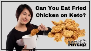A young woman debating if she can eat fried chicken on a low carb diet and who is wearing a black sweater while holding a white bucket of fried chicken with a large smile on her face and beside her is several fried chicken legs and thighs.