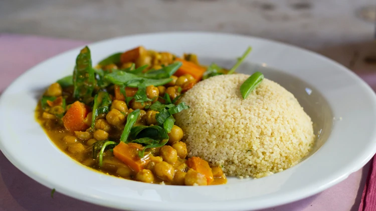On a white ceramic plate is a chickpea and couscous vegan curry meal served on top of a pink surface.