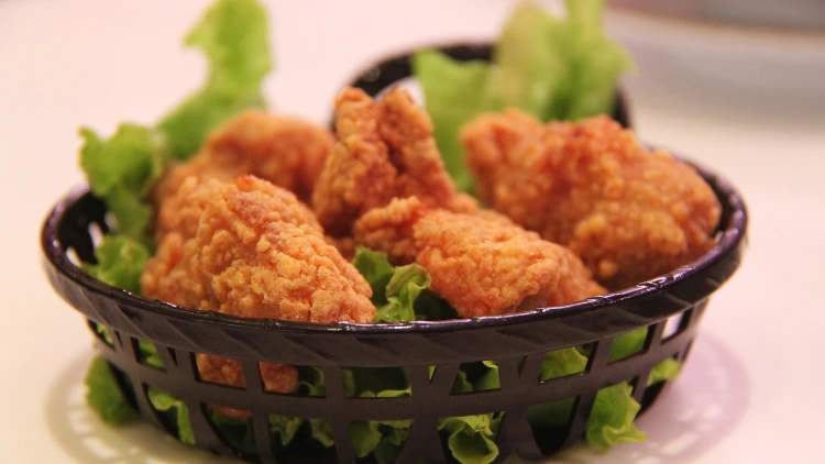 A black basket that contains pieces of fried chickens with lettuces and placed on top of a matte white surface.