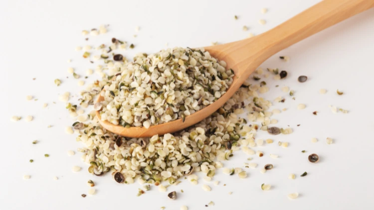A wooden spoon full of hemp seeds that is also spilled all over the white surface.
