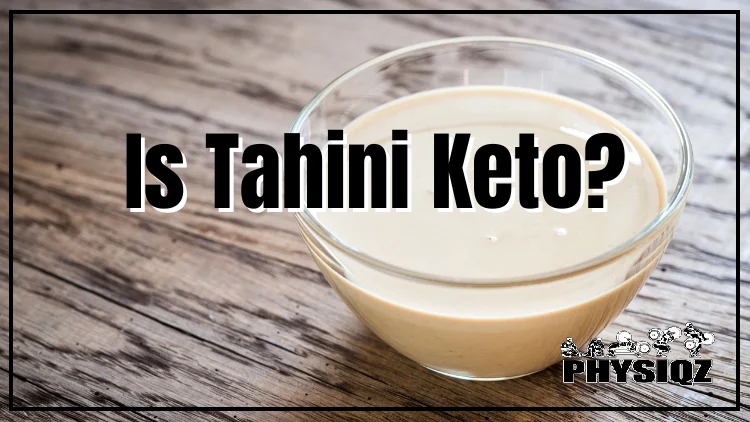 A small clear bowl filled with creamy tahini sauce that's on off white to yellow-ish color and it's resting on a wooden surface.